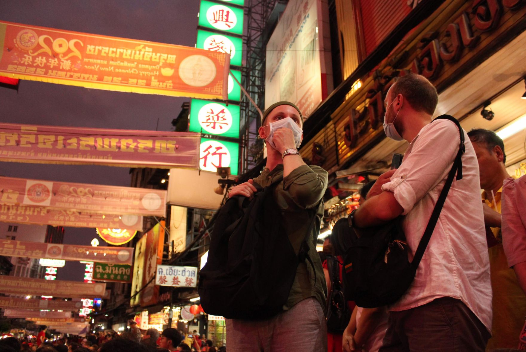 Two men wear masks under the lights in a downtown Bangkok market